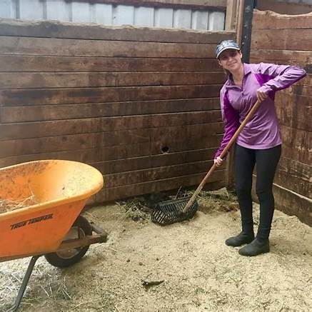 A volunteer mucking out a stall in the barn