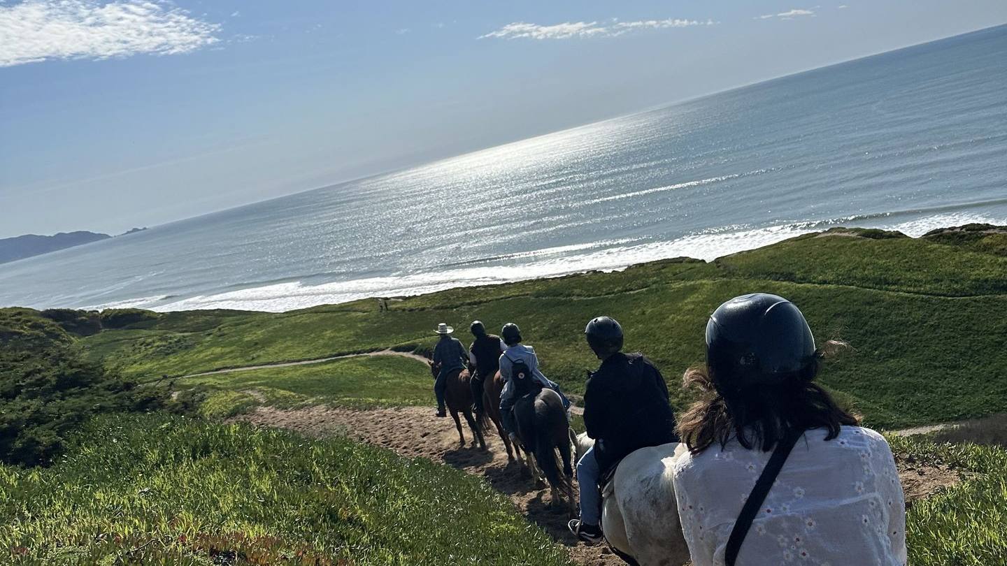 Riders strung out along a green coastal trail high above the ocean south of San Francisco