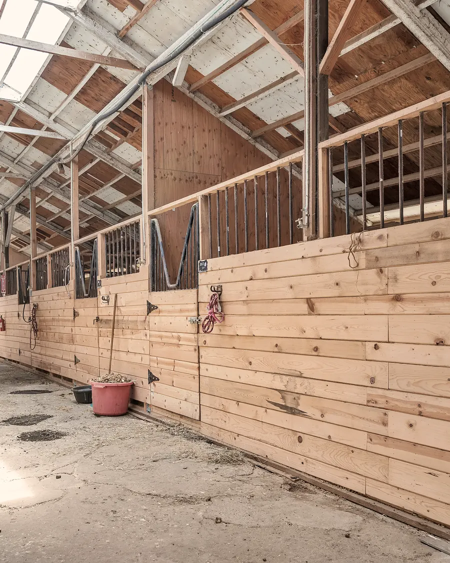 A quiet barn aisle at Ocean View Stables, stall doors closed and a bucket by the wall